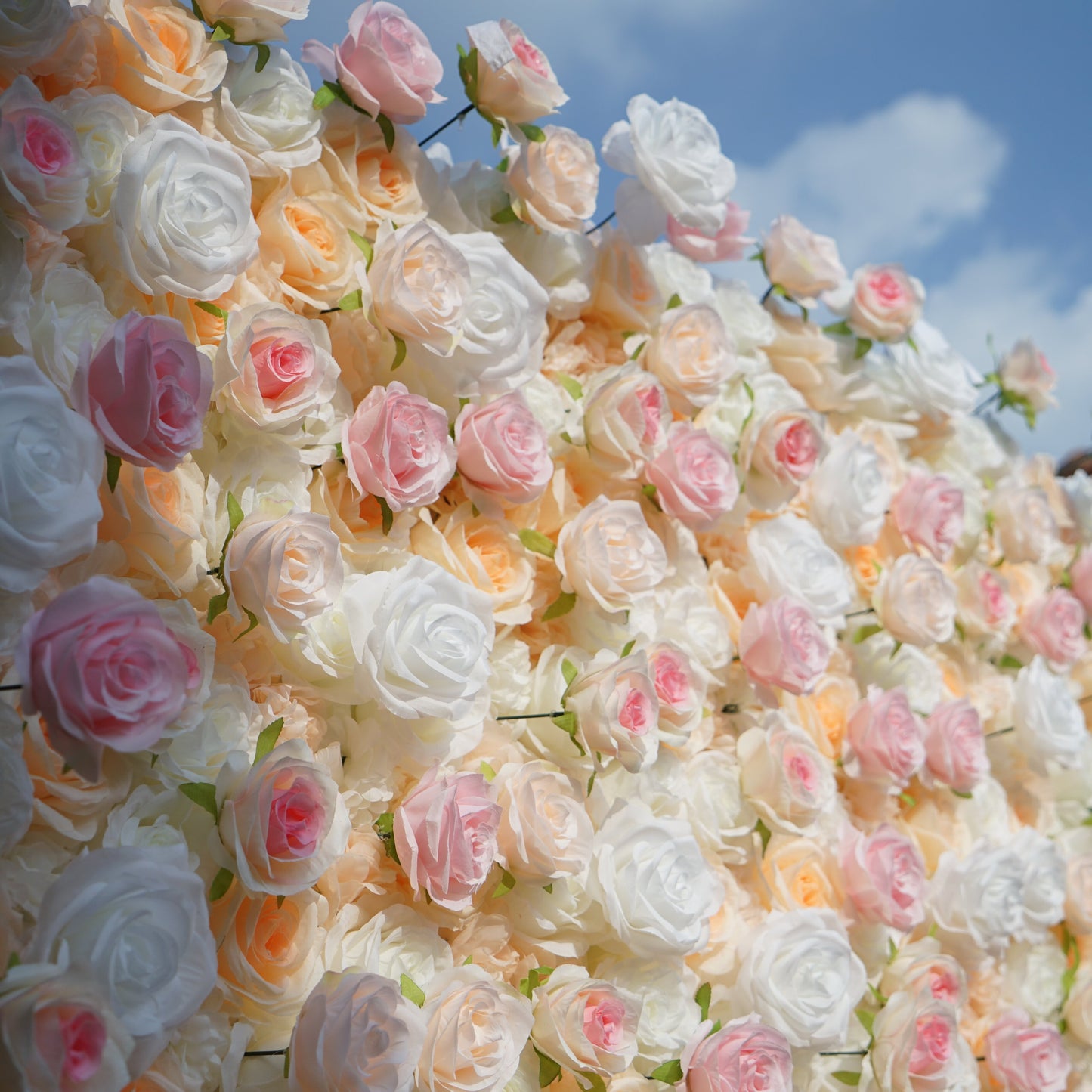 Wall of artificial roses in pastel colors against a blue sky.